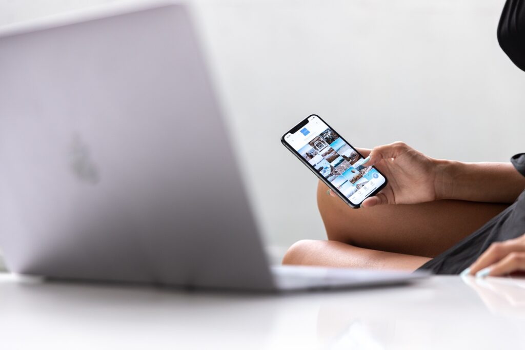 hands holding a mobile phone and a laptopn on the desk