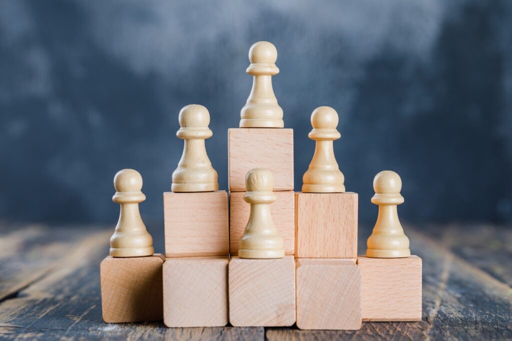 business strategy concept with chess figures on toy wooden ladder on foggy and wooden background side view.